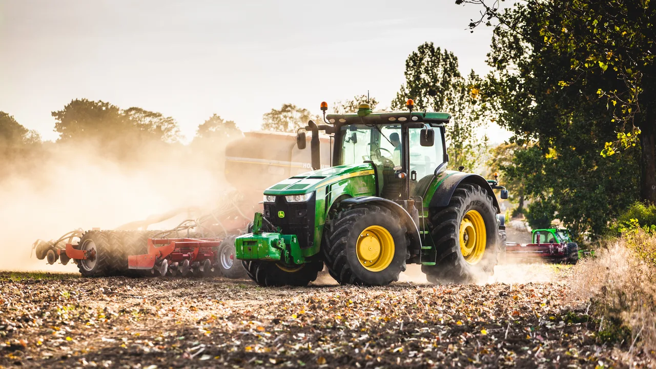Ciągnik John Deere wykonuje jesienne prace polowe.