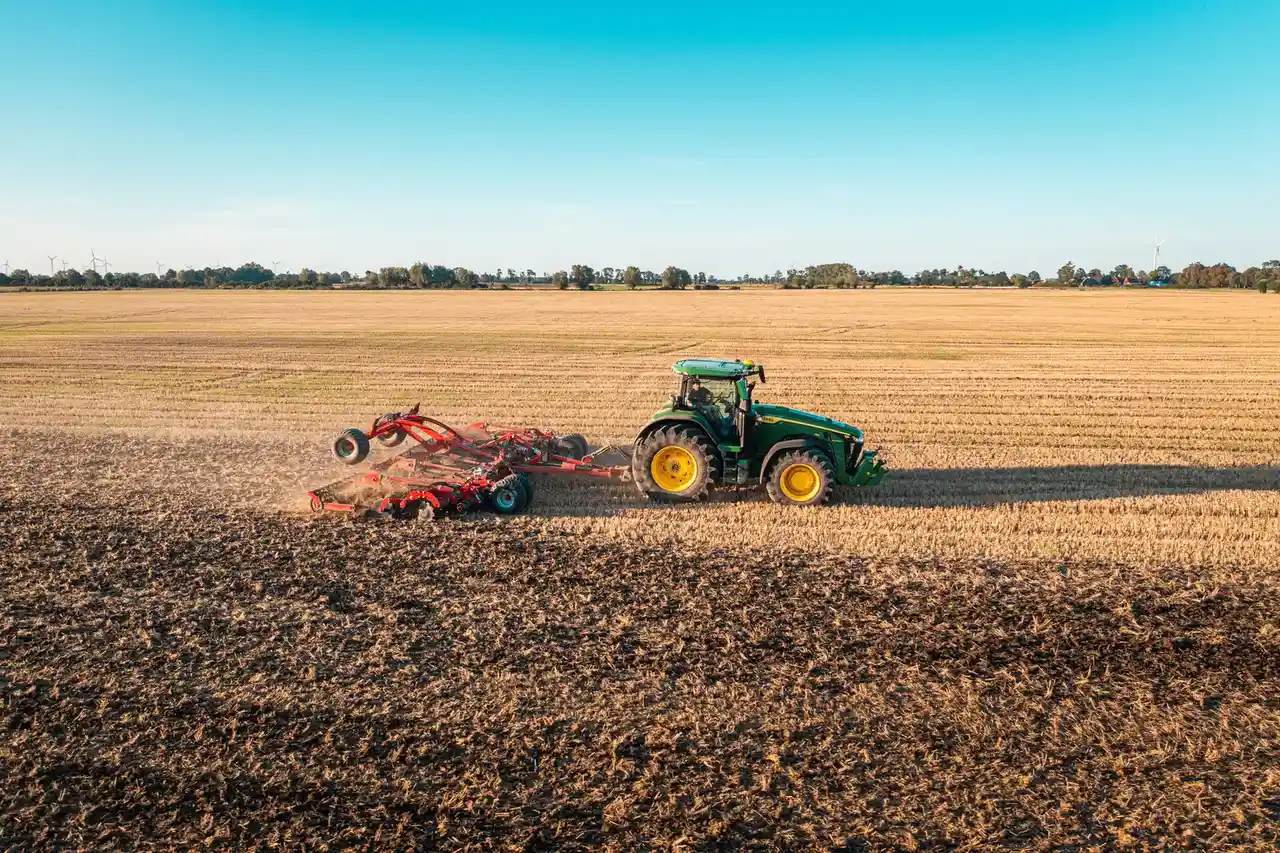 Ciągnik John Deere ciągnie agregat uprawowy po polu.