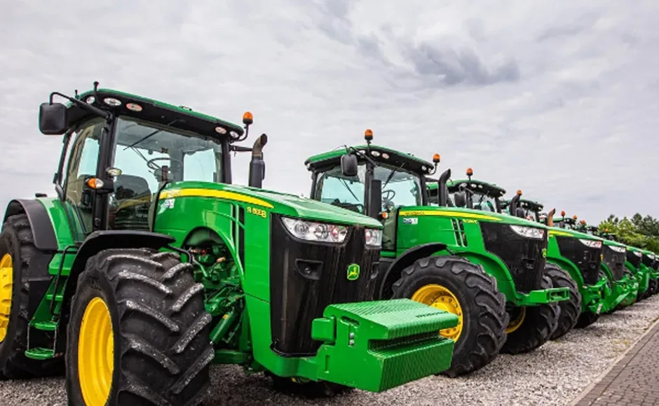 Ciągniki John Deere stoją na placu maszyn rolniczych.